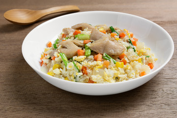 close up of fried rice with chicken and vegetables in a ceramic plate on wooden table. homemade style food concept.
