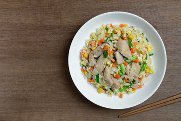top view of fried rice with chicken and vegetables in a ceramic plate on wooden table. homemade style food concept.