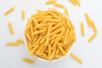 Dried penne Italian pasta in a round bowl ready to be cooked, isolated on white table, with view from above 