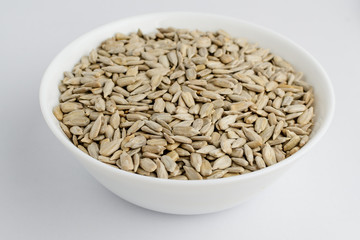 Freeh raw organic sunflower seeds in a white round bowl on a table in soft focus, isolated on white, top view