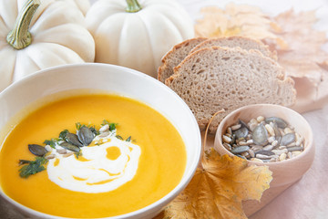 Seasonal food.Pumpkin soups. Soup decorated with cream sauce and pumpkin seeds. White background .Autumn foliage