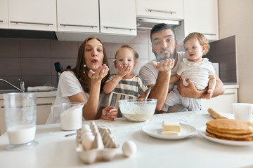 funny family having fun in the kitchen, parents and kids blowing flour, close up photo. entertainment concept