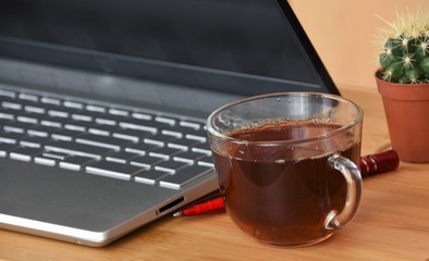 laptop, cactus, pen and glass mug with tea