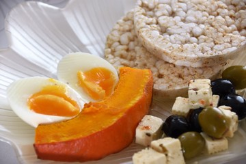 healthy breakfast, olives, cheese, rice, waffles, baked pumpkin and chicken egg on a white plate