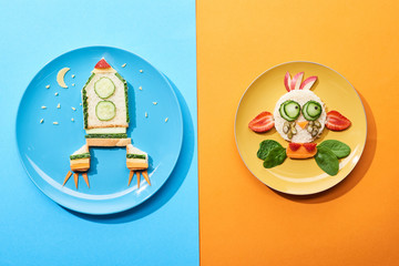 top view of plates with fancy face and rocket made of food for childrens breakfast on blue and orange background