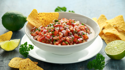 Mexican Tomato Salsa in white bowl with lime, red onion, jalapeno pepper, parsley and tortilla chips