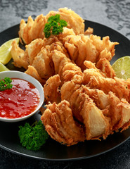 Fried Bloomin Onion with Chilli sauce and lime on black plate