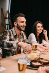 selective focus of young man taking chips from bowl while sitting with friends in pub