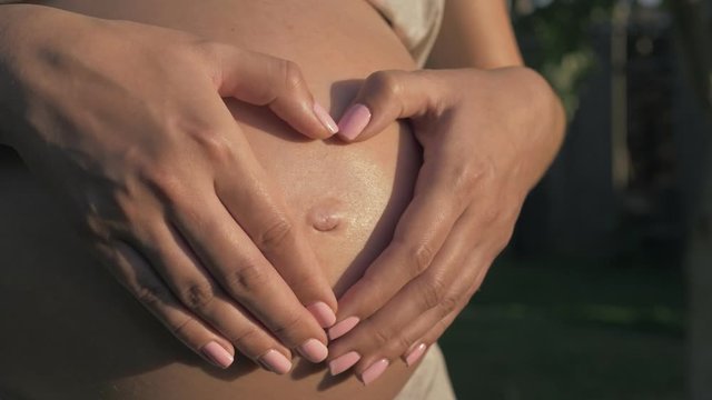 Pregnant Woman Makes A Heart On Her Stomach With Her Hands In Light Of Sunset