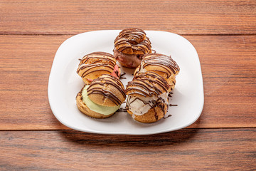 Profiteroles with ice cream and chocolate. Eclairs with black chocolate on wooden background. Traditional French dessert.