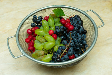 bunches of black and green grapes and red berries of hawthorn in a metal basket