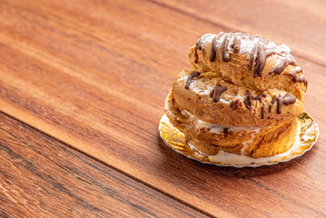 Profiteroles with ice cream and chocolate. Eclairs with black chocolate on wooden background. Traditional French dessert.
