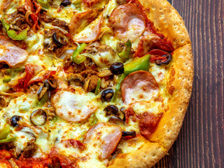 Pizza with meat, cheese and olives on a wooden table