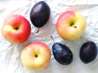 Red and yellow apples and prunes on white wrapping paper