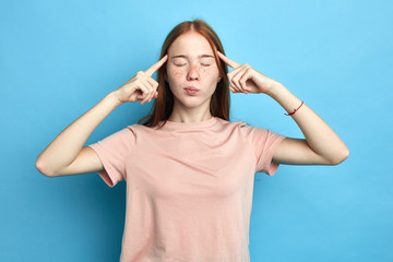 depressed frustrated upset serious girl concentrated on thinking, trying to remember something, woman has terrible headache, girl massaging her temples. close up portrait. isolated blue background