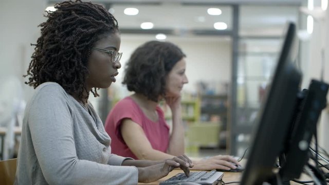 Side view of two women working with computers. Concentrated ladies using computers at public library. Technology concept