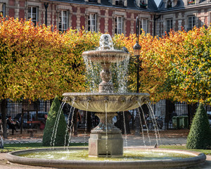One of the four Cortot fountains in the beautiful Place des Vosges in Paris, France with colorful Autumn trees in background.