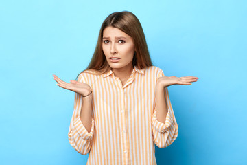 unsure puzzled young woman spreads palms in bewilderment, girl has puzzled facial expression, isolated blue background, reaction, facial expression, student doesn't know the answer of the question