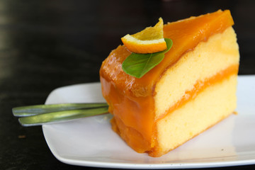 Orange cake in white dish with spoons on black background.