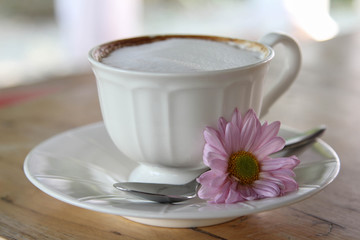 Hot cappuccino coffee in white cup decorated with purple daisy flower.