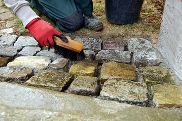 pavement works, Cobbled pavement natural stone. gloved Hands of worker cleaning concrete paver...