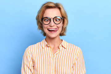 Close up positive portrait of pretty crazy girl with short fair, , showing long tongue.close up portrait, isolated blue background, studio shot. craziness, joy