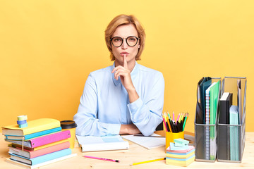 serious businesswoman with a finger on her lips, showing silence gesture, teacher asking students to calm down, stop talking. close up portrait, isolated yellow backgroun, body language.