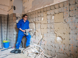 Plumber in a work of a kitchen, chopping the wall of a kitchen.
