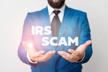 Text sign showing Irs Scam. Business photo showcasing targeted taxpayers by pretending to be Internal Revenue Service Man with opened hands in fron of the table. Mobile phone and notes on the table