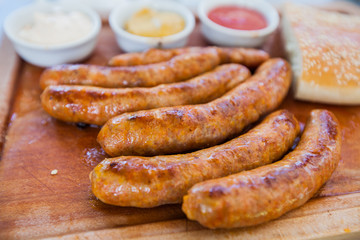 Tasty grilled sausages with sauce and bread on wooden board served at restaurant table