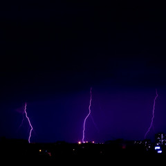 Naklejka na ściany i meble Three lightning strikes in a row. Mysterious violet glowing sky above the night Odessa city. Night city lights before the thunderstorm.