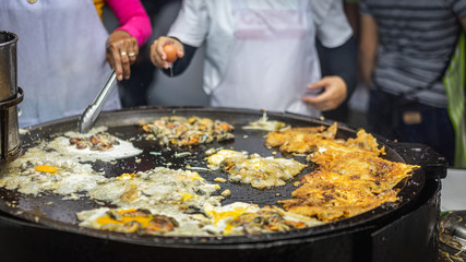 Hand of chef cooking Oysters fried in egg batter in hot flat pan,Cooking, at night market, street food Thailand, Bangkok