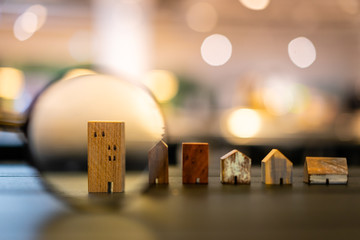 Hand holding magnifying glass and looking at house model, house selection, real estate concept.
