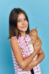 smiling happy brunette girl has found stray kitten, close up portrait, isolated blue background.
