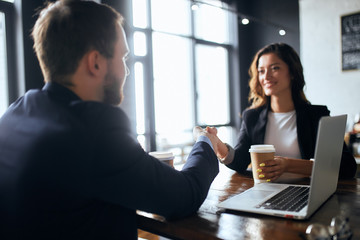 cheerful brunette woman and brow-haired bearded man shaking hands during business meeting. close up photo