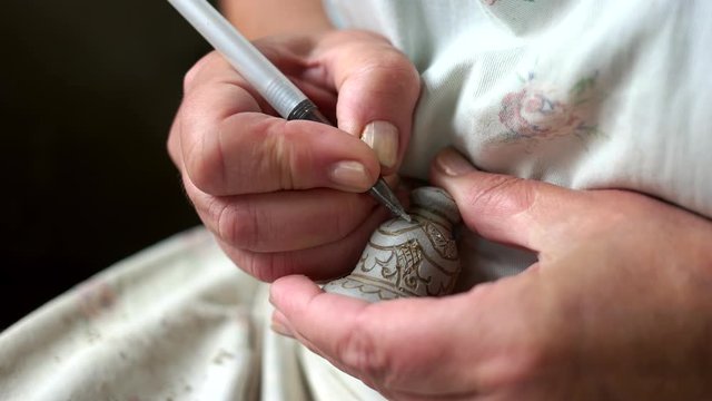 Close up of man decorating clay figure. Potter decorating clay product with painting. Creativity concept.