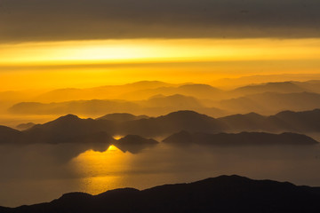 Mediterranean landscape. Sunset on the sea with flowing bright colored rays of the sun through the clouds. Silhouettes of mountains.  Background, blur.