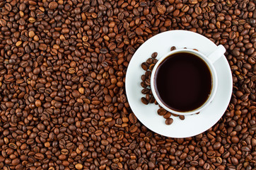 Background of roasted coffee beans. In the foreground is a white coffee Cup on a saucer of coffee.