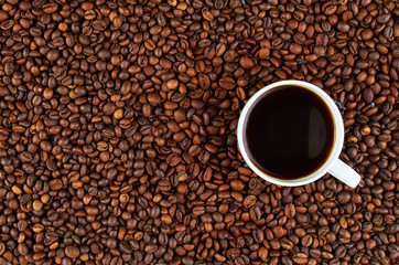Background of roasted coffee beans. In the foreground is a white coffee Cup with coffee.