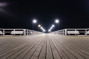 Wooden pier by the sea lit by lamps at night. - obrazy, fototapety, plakaty