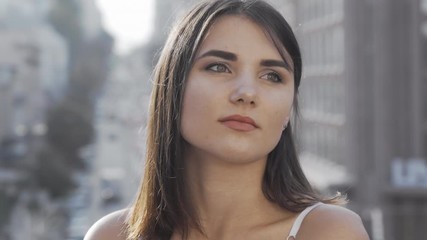 Beautiful woman looking away while waiting someone to meet in the city. Attractive young female looking around on city background. Charming female cropped portrait