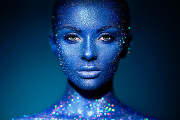 Fashion model woman in blue bright sparkles and neon lights posing in studio. Portrait of beautiful...