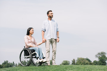 Fototapeta premium handsome young man holding hands with disabled girlfriend sitting in wheelchair