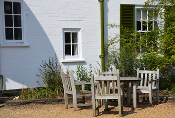 Wooden table and chairs in the outdoor patio next to a white brick house