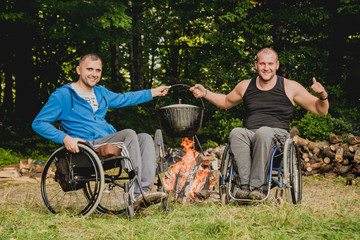 Two disabled men resting in a campsite with friends. Wheelchair in the forest on the background of...