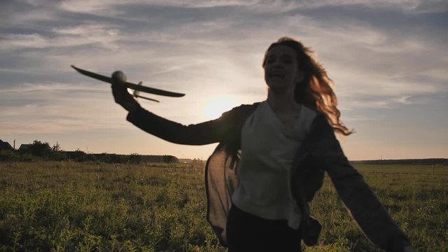 A young girl runs with a toy airplane against the sunset sky.