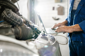 Motor of broken lorry and hands of experienced technician touching laptop keys