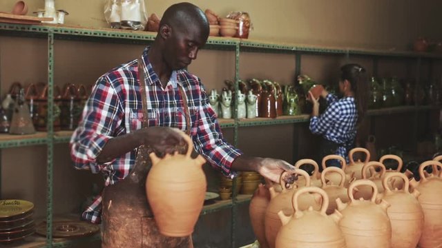 Woman and man artisans in apron having ceramics in store warehouse