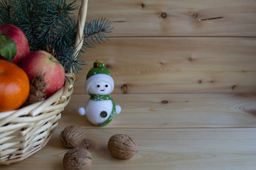 Christmas composition in a basket with oranges, apples, Christmas tree and snowman, on a warm wooden background, the concept of the holiday