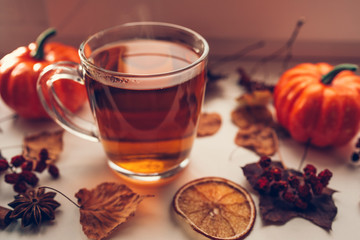 Hot steaming Cup of tea with autumn leaves, pumpkins and spices on the windowsill. Autumn mood.